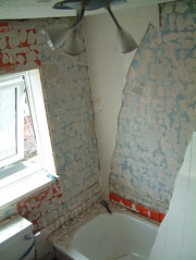 Sections of wall with tiles removed, some tiles remaining and a bolster on the bath